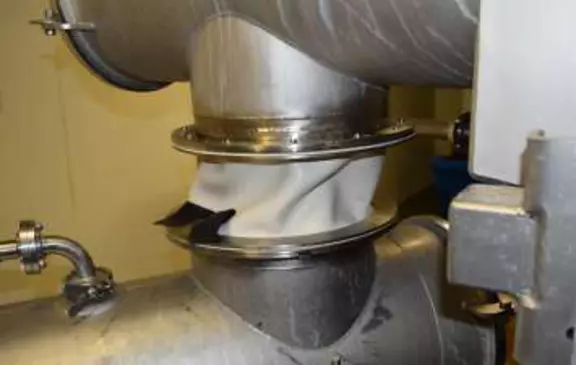 White fabric expansion joint installed in a stainless steel process system for flexible movement compensation in hygienic industrial applications.
