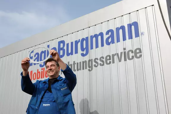 Technician in EagleBurgmann uniform smiling and holding a seal ring in front of a mobile sealing service unit.
