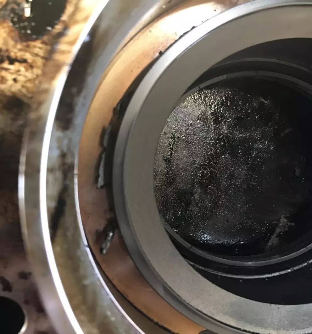 A close-up view looking into a dirty industrial machine component, showing concentric metal rings, one with signs of wear or damage, and a heavily soiled, dark interior.