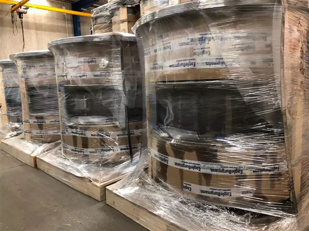 Pallets stacked with large, cylindrical industrial components, wrapped in clear plastic stretch film with "EagleBurgmann" logo tape visible on the cardboard packaging.