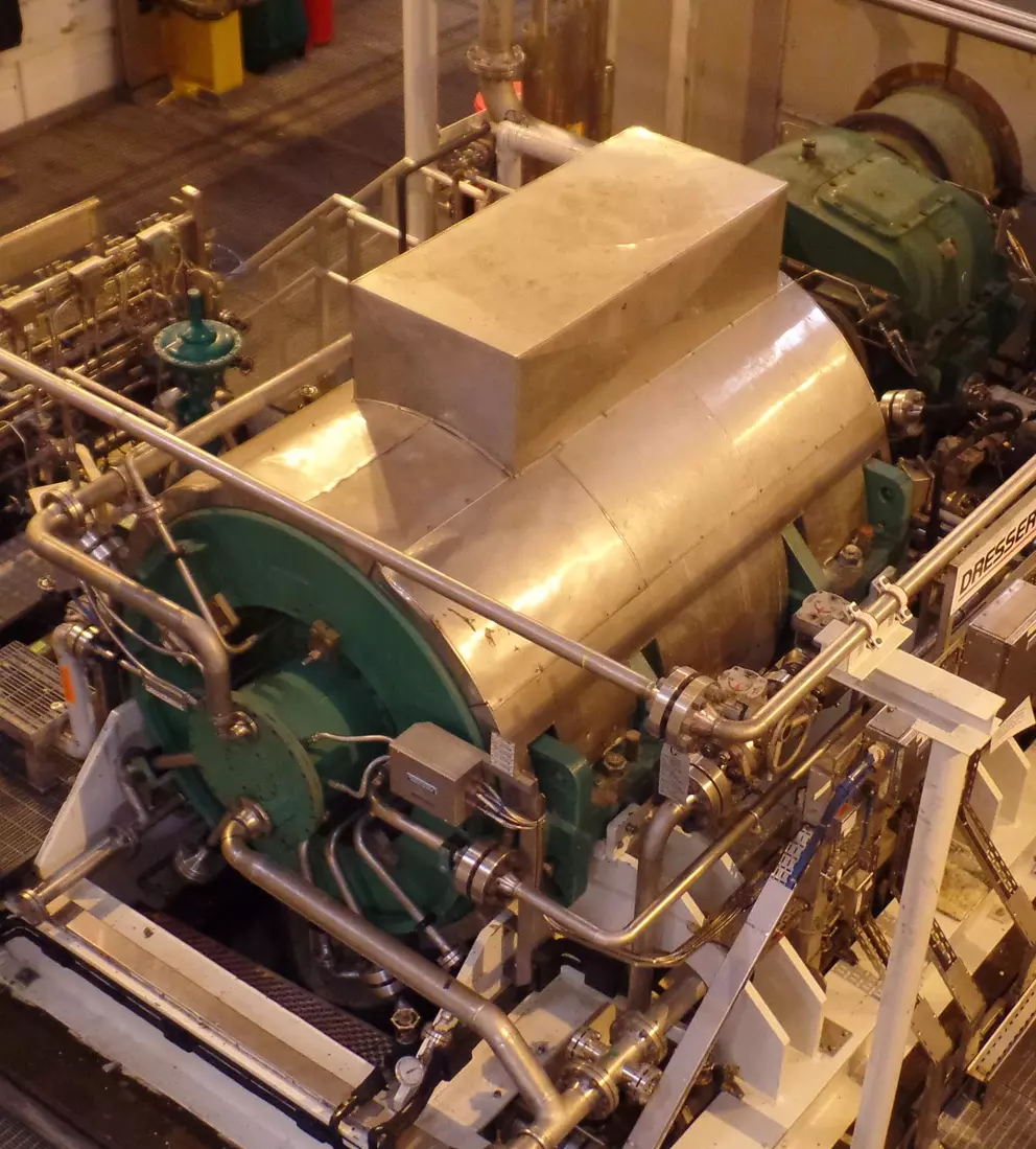 Close-up view of industrial machinery with metal piping and a large cylindrical component in a factory setting.