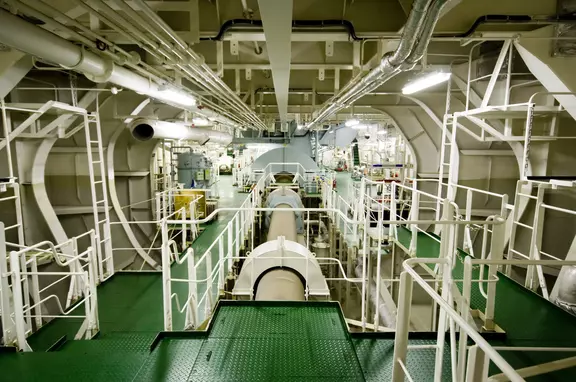 Interior of an industrial engine room with piping, platforms, and rotating equipment.