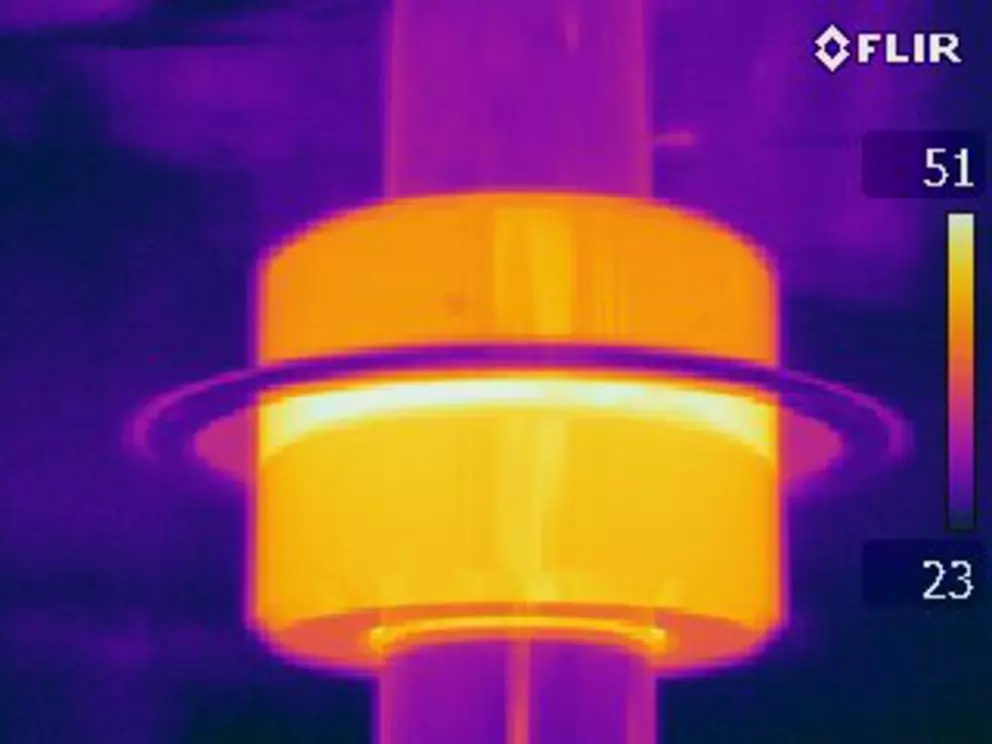 A thermal image showing a cylindrical component on a shaft glowing bright yellow and orange, indicating high heat, against a purple background, with a temperature scale on the right.