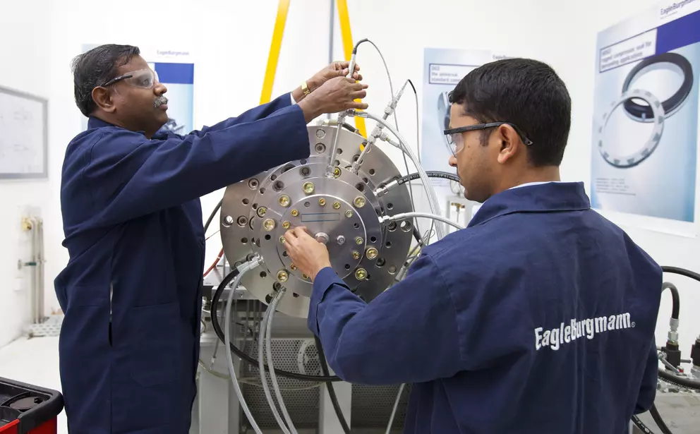 Zwei Techniker installieren oder prüfen eine große industrielle Gleitringdichtung an einem Prüfstand, umgeben von Messleitungen und Anschlüssen.