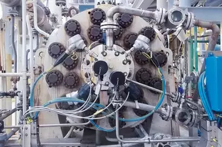 Nahaufnahme eines großen Industriekompressors mit mehreren Rohranschlüssen, Ventilen und Messtechnik, wie er in einer Verarbeitungsanlage eingesetzt wird.