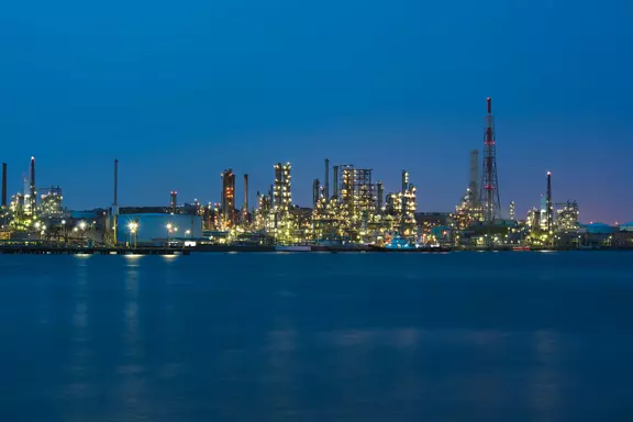 Industrial refinery complex illuminated at night, showing large-scale energy processing and petrochemical operations near the water.