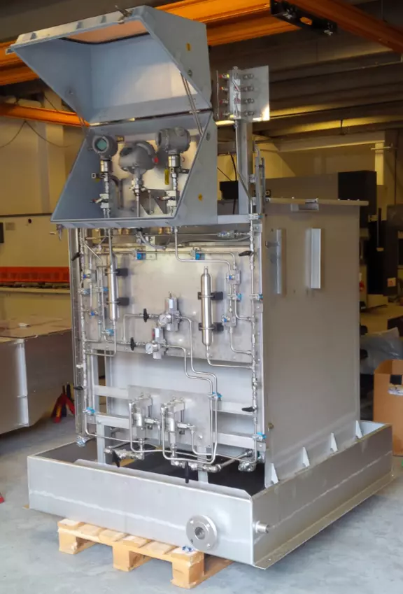 Industrial process control unit with stainless steel piping, instrumentation, and containment base in a manufacturing environment.