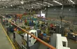 Wide view of an industrial production facility with machining stations, work areas, storage shelves, and technicians, highlighting large-scale manufacturing and workshop operations.