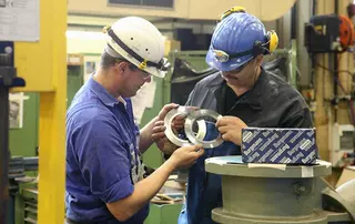 Zwei Techniker mit Schutzhelmen überprüfen präzise gefertigte Dichtungskomponenten in einer Werkstatt.
