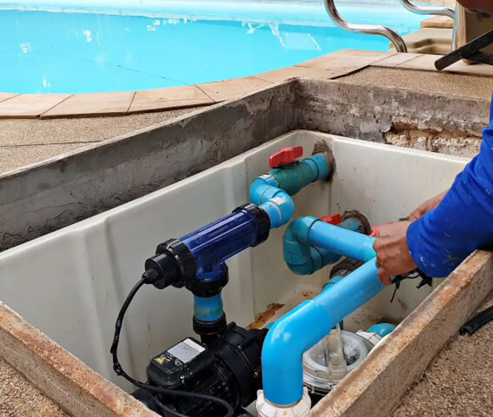 Techniker bei der Wartung eines Schwimmbad-Pumpensystems mit blauen PVC-Rohren und Filtereinheit.