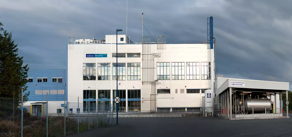 Vistin Pharma industrial building with large windows and external piping, under a cloudy sky.