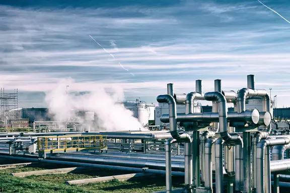 Industrial CO₂ processing and transport facility with insulated stainless steel pipelines, steam release, and storage tanks under a clear sky.