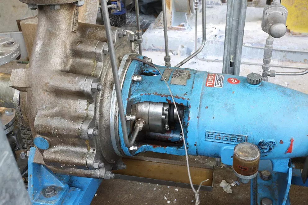 A close-up of a partially disassembled industrial centrifugal pump, showing the gray metal casing of the pump end bolted to a worn, bright blue section that contains the mechanical seal and shaft. The pump is branded "TURBO EGGER."