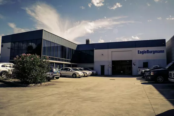 EagleBurgmann facility with modern industrial architecture, parking area, and company signage under a bright sky.