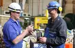 Two EagleBurgmann technicians in a workshop exchanging and inspecting a mechanical seal component, highlighting teamwork, technical expertise, and industrial service operations.
