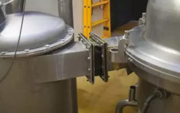 Compact fabric expansion joint connecting stainless steel process vessels for vibration isolation and flexible movement in hygienic industrial systems.