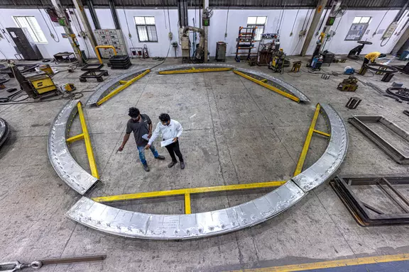 Engineers reviewing a large circular industrial expansion joint structure in a fabrication workshop for heavy-duty plant and ducting systems.
