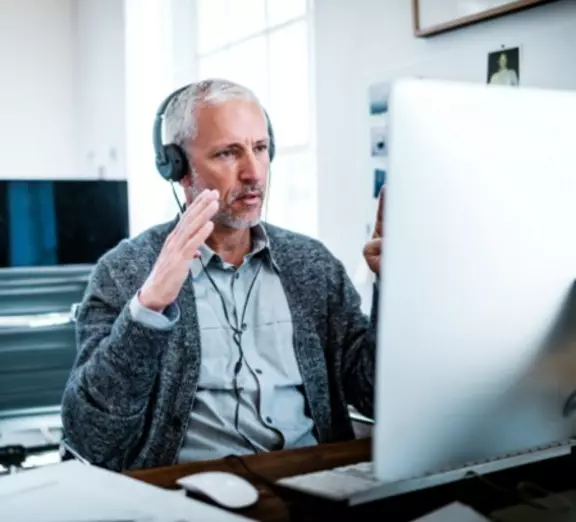 Professional in a video call wearing a headset at a desktop computer in an office setting.