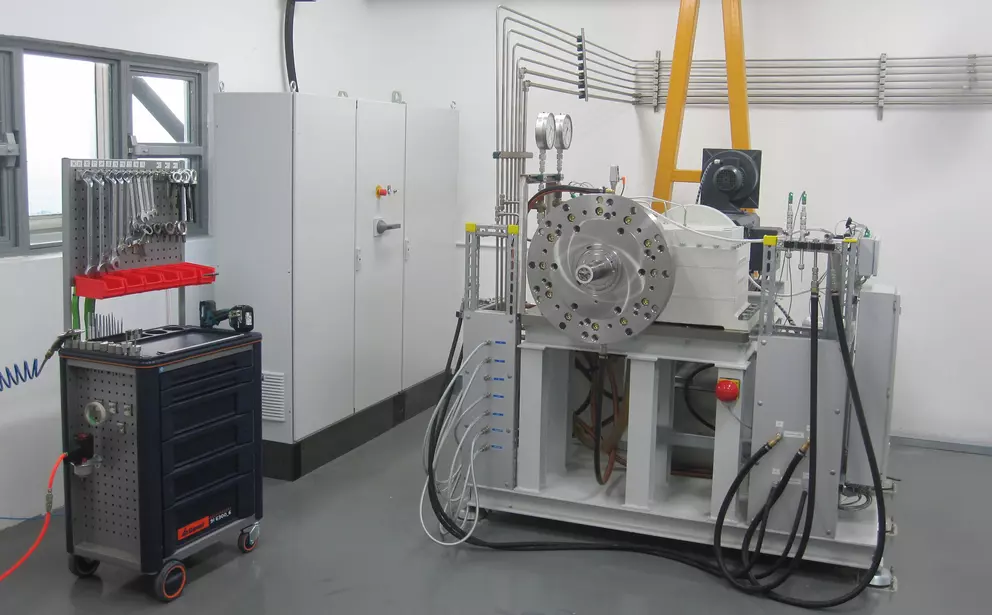Industrial test bench for mechanical seals with hydraulic lines, control systems, and a connected mobile supply cart in a technical laboratory environment.