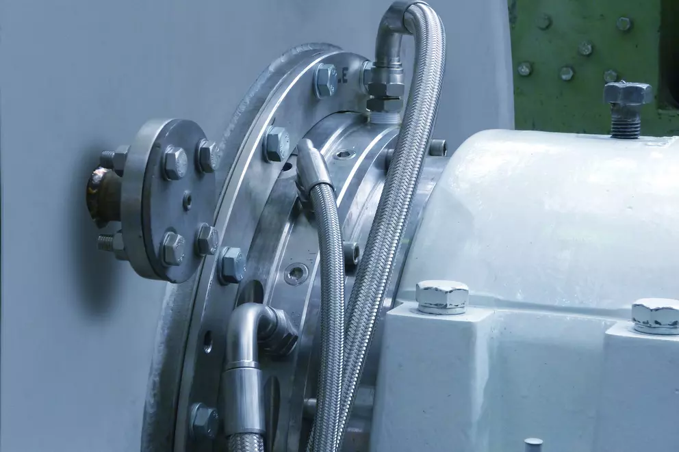 Mechanical seal connection on industrial equipment housing with flexible tubing.