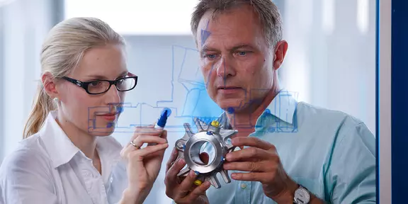 Technical experts examining a precision-engineered metal part – collaborative design and development in mechanical engineering and sealing technology.