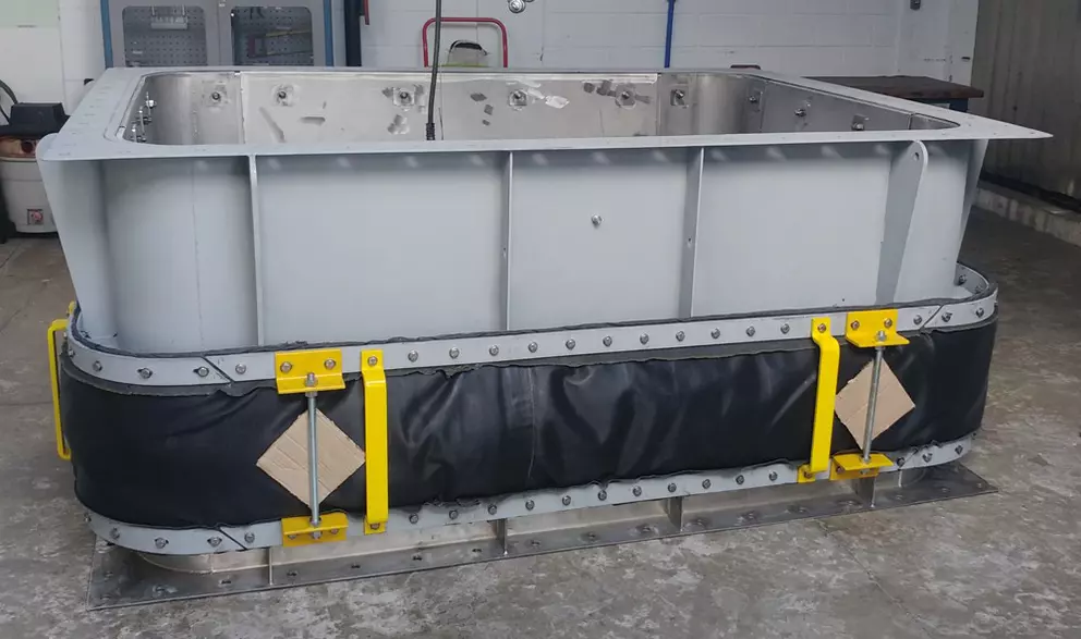 Großes rechteckiges industrielles Metallgehäuse oder Kanalabschnitt mit einer schwarzen flexiblen Dehnungsfuge, die um den Sockel gewickelt ist.