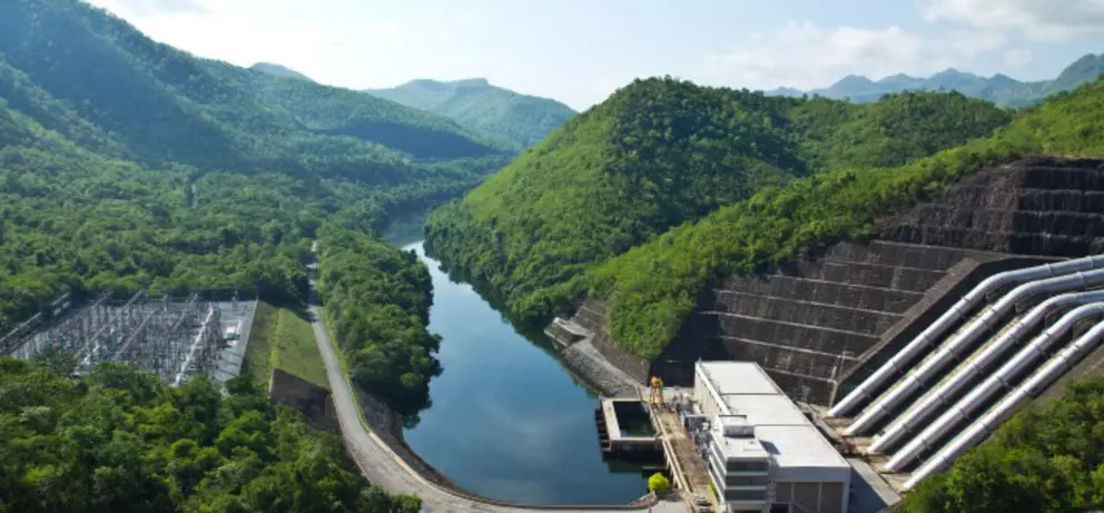 Hydropower dam facility with large water pipelines surrounded by lush green mountains and a river valley.