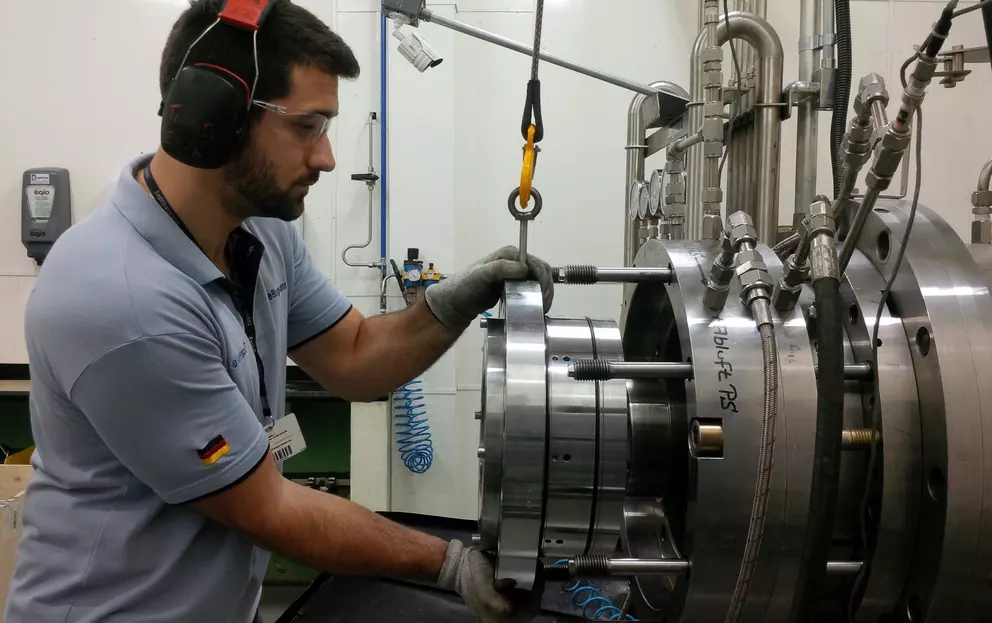 Techniker montiert eine große industrielle Gleitringdichtung an einem Prüfstand und verwendet dafür einen Hebezeughaken.
