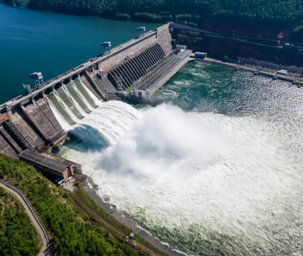 Large hydroelectric dam releasing water for power generation surrounded by forest and reservoir.