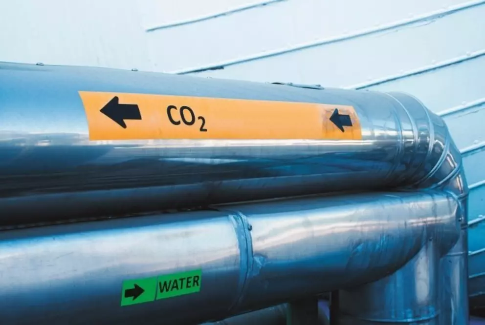 Industrielle Metallrohrleitungen, die mit CO₂ und Wasser gekennzeichnet sind und den Fluss bzw. die Transportrichtung anzeigen.