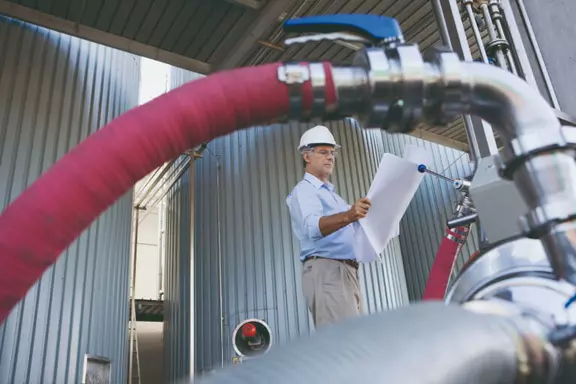 Engineer inspecting an industrial plant with pipelines and blueprint in plant engineering.