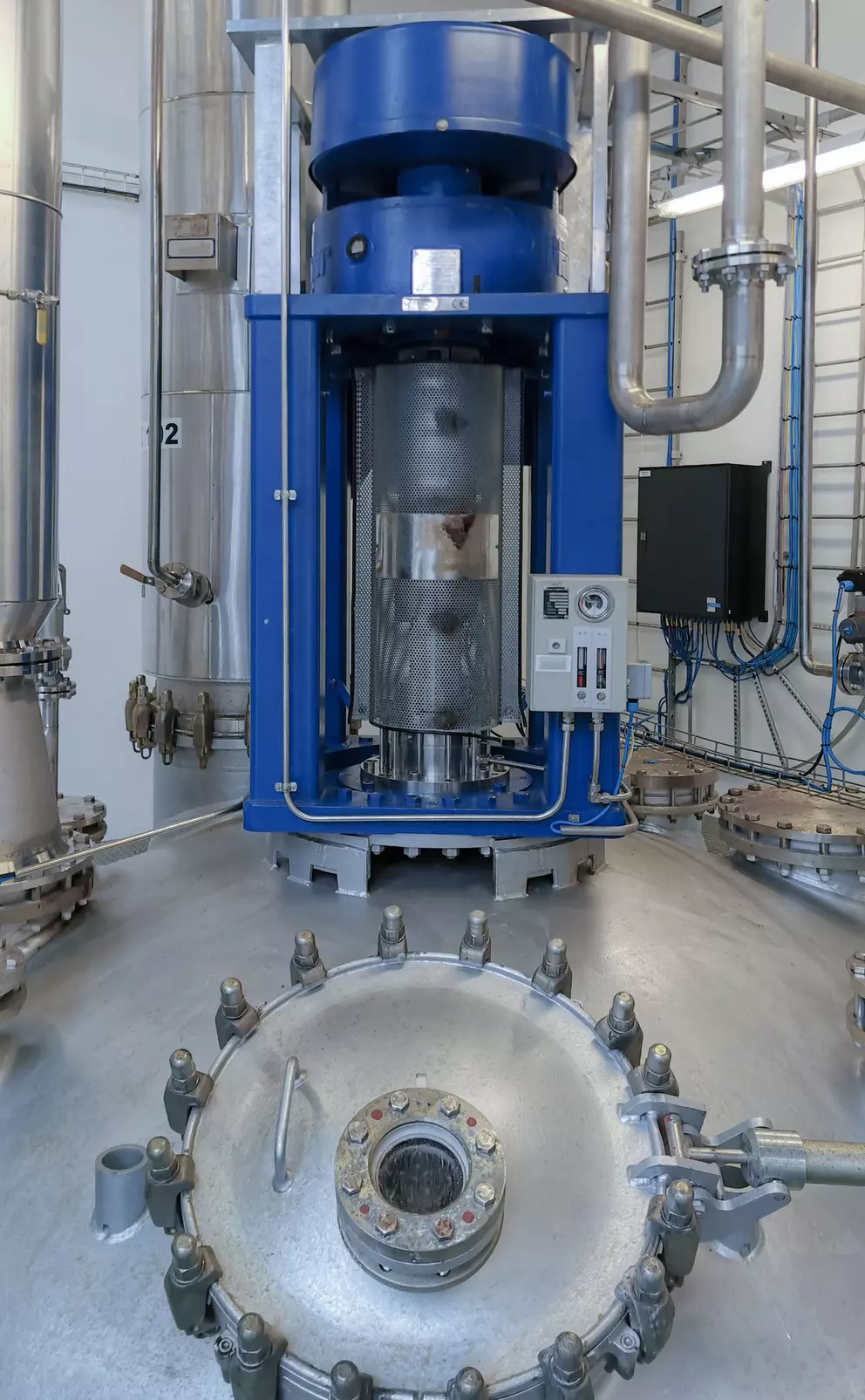 Industrial reactor vessel with a blue vertical agitator, surrounded by pipes and control equipment in a processing facility.