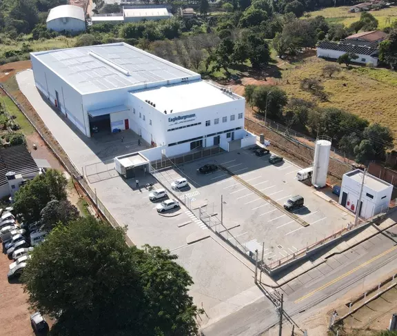 Vista aérea da unidade da EagleBurgmann no Brasil com área de armazém, área de escritório, estacionamento e terreno industrial cercado.