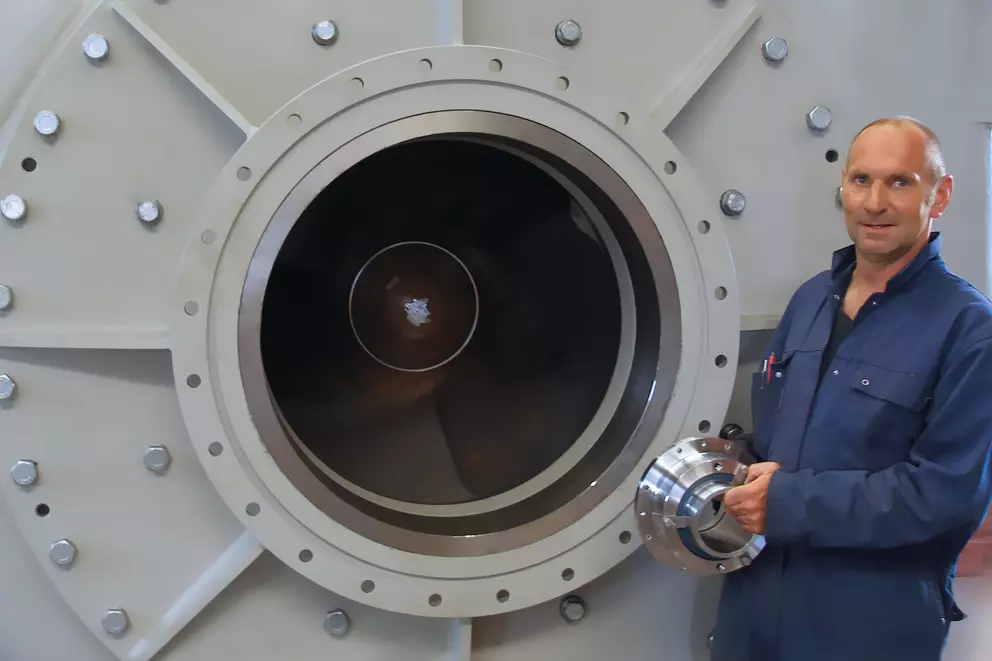 Employee standing in front of a large pump system holding a component for dredger pump applications.