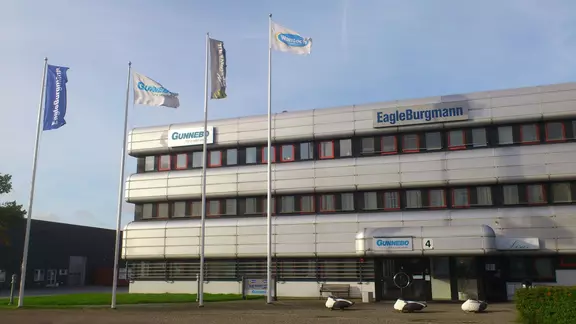 EagleBurgmanns kontorsbyggnad med företagsskylt och flaggstänger framför en modern kommersiell fasad.