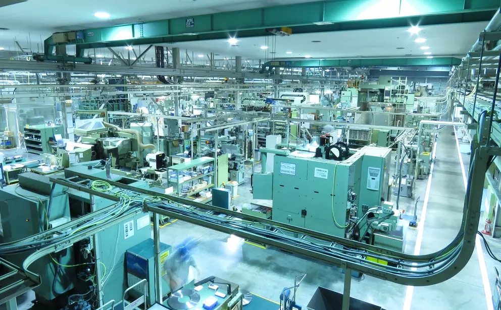 Moderne industrielle Fertigungshalle mit automatisierten Anlagen, Förderstrecken und komplexen Produktionssystemen.