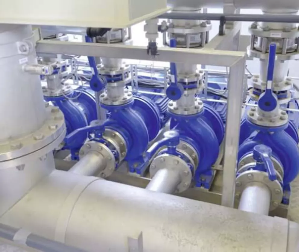 Industrial pump system with blue valves and stainless steel pipes in a water treatment facility.