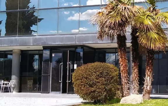 Modern EagleBurgmann office entrance with glass facade, palm trees, and landscaped greenery.