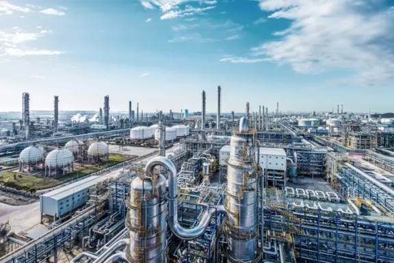 Large industrial petrochemical plant with storage tanks, pipelines and refinery towers under a clear sky.