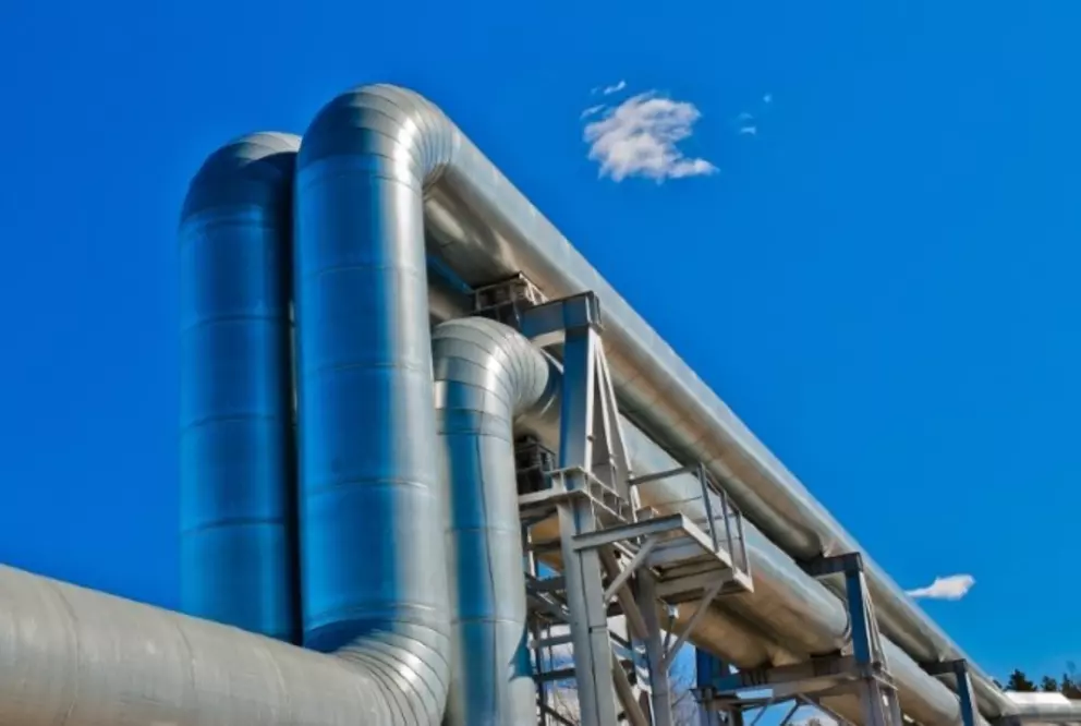 Large industrial piping system against a clear blue sky, representing energy or chemical processing infrastructure.