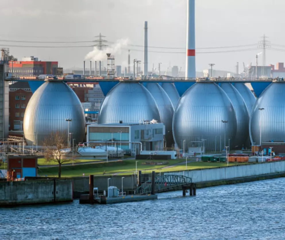 Modern wastewater treatment plant with large silver biogas digesters beside an industrial river.
