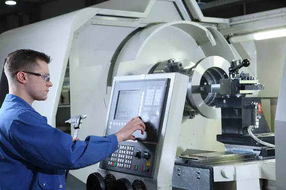 Technician operating a CNC lathe in an industrial manufacturing environment.
