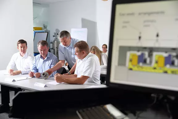 Teilnehmer einer technischen Schulung analysieren eine mechanische Dichtung, während Schulungsinhalte auf einem Monitor gezeigt werden.