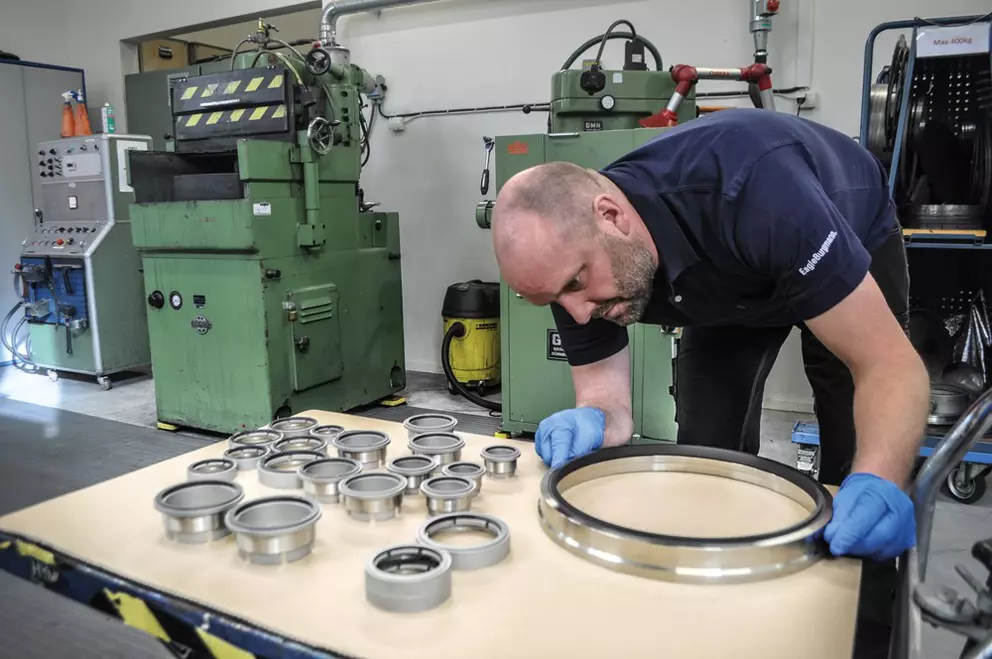 Technician inspects metal seal ring on a worktable in an industrial workshop.