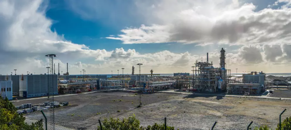 Industrial plant near the coast with metal structures and cloudy sky in the background.