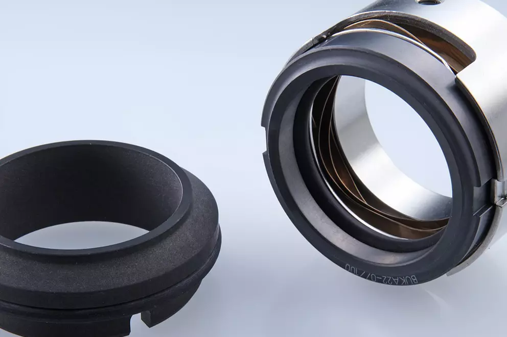 A close-up of two mechanical seal components: a dark, black carbon or ceramic stationary ring on the left, and a multi-part rotating assembly, featuring metal and rubber, on the right.