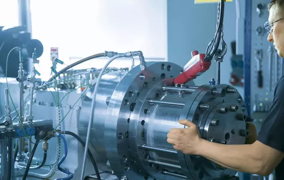Techniker richtet eine große industrielle Prüfvorrichtung mit hydraulischen Leitungen und Sensoren aus.