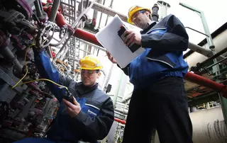 ngenieure mit Schutzausrüstung inspizieren industrielle Rohrleitungssysteme und erfassen Wartungsdaten in einer Verarbeitungsanlage.