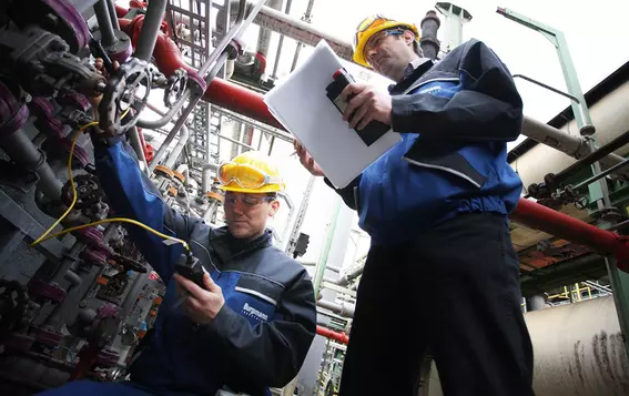 ngenieure mit Schutzausrüstung inspizieren industrielle Rohrleitungssysteme und erfassen Wartungsdaten in einer Verarbeitungsanlage.