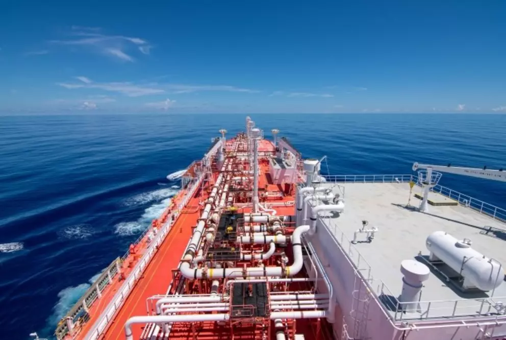Top view of an LNG carrier at sea showing complex piping and gas handling systems on deck under clear blue sky.